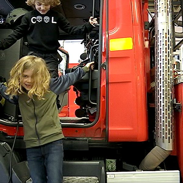 Två barn hoppar ner från förarsätet på en brandbil.