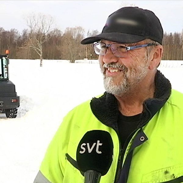 en leende man står på isen, liten traktor i bakgrund