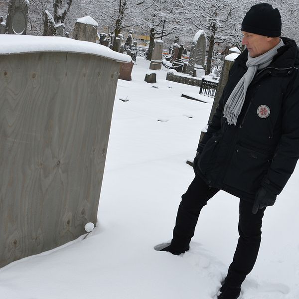 Kyrkogårdschefen Torleif Örn står på en snöig kyrkogård och tittar på en låda av trä som satts utanpå en gravsten. På toppen av lådan har några centimeter snö samlats.