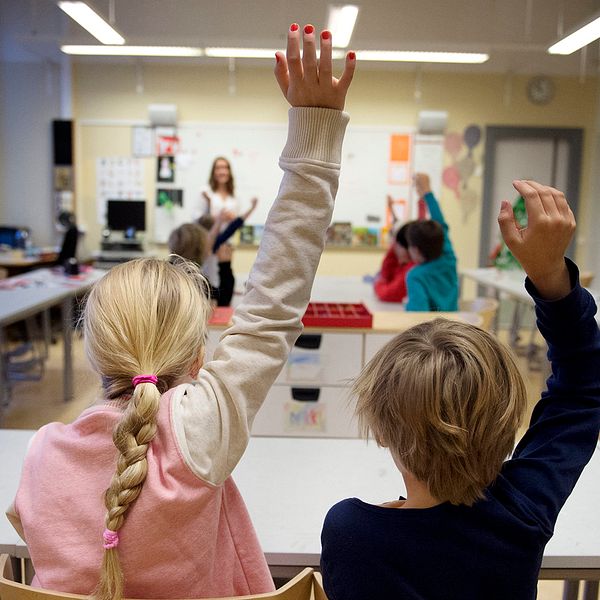 Barn i ett klassrum som räcker upp sin hand.