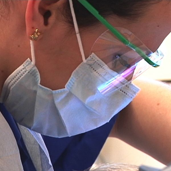 En kvinna med vårdkläder och munskydd hjälper en patient.