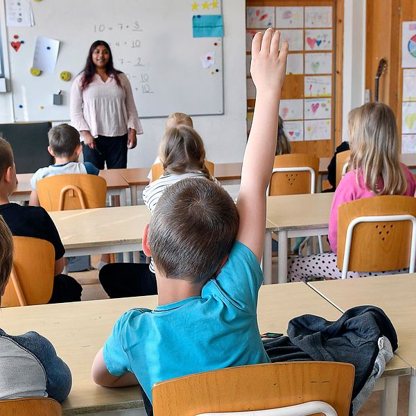 ung abarn i klassrum, kvinnlig lärare framme vid tavlan