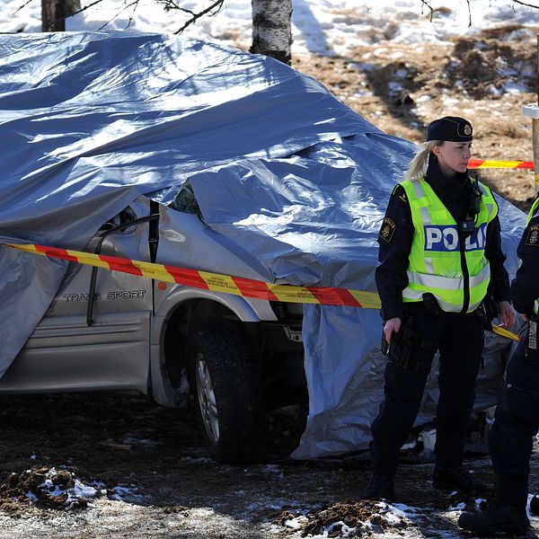 Två poliser står framför en silvrig bil som är täckt med en presenning