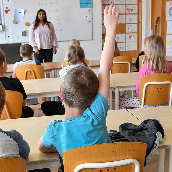 unga skolbarn i klassrum, lärare framme vid tavlan