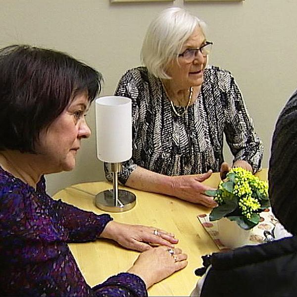 Två kvinnor från Asylkommittén vid ett bord med en asylsökande som sitter med ryggen mot kameran.