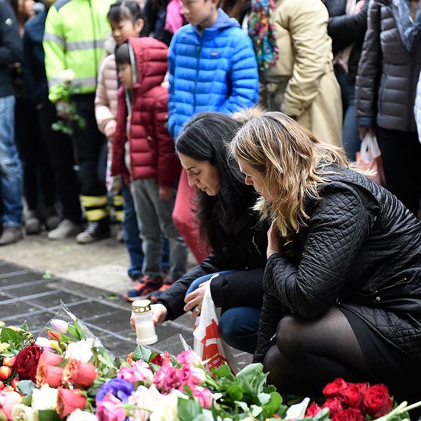 Två kvinnor står hukade framför ett blomsterhav för att hedra de som drabbades av terrorattacken på Drottninggatan i Stockholm 2017