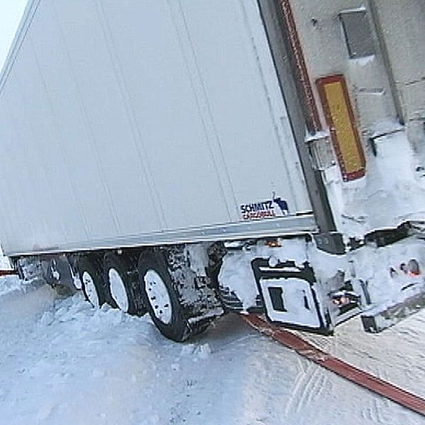 lastbilssläp som står halvvägs ner i diket på vinterväg