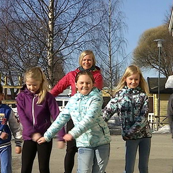 fem barn och en vuxen i en dansrörelse på skolgård