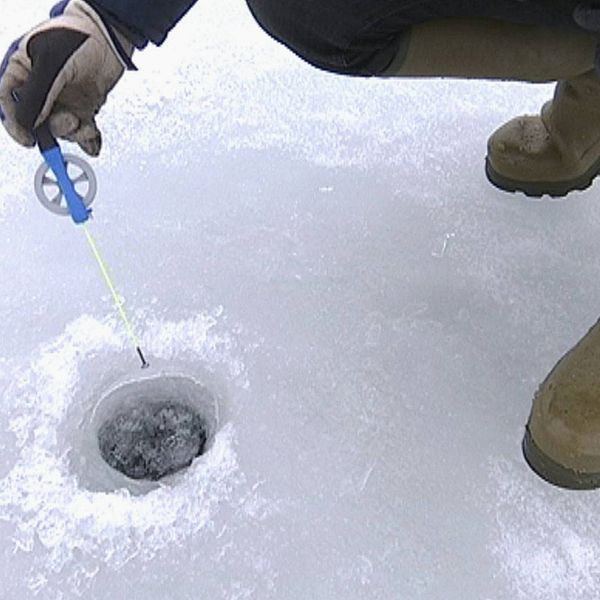 foto neråt som visar hand som håller pimpelspö ner mot ett hål i isen, och fötterna på person