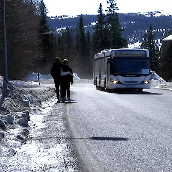 Två person tvingas gå längs bilväg eftersom det saknas gångväg, möter buss.