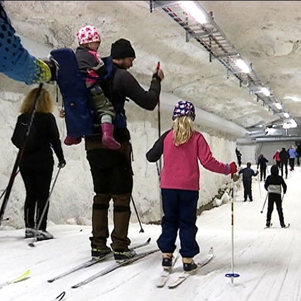 Vuxna och barn åker skidor inne i en tunnel med snö och skidspår.