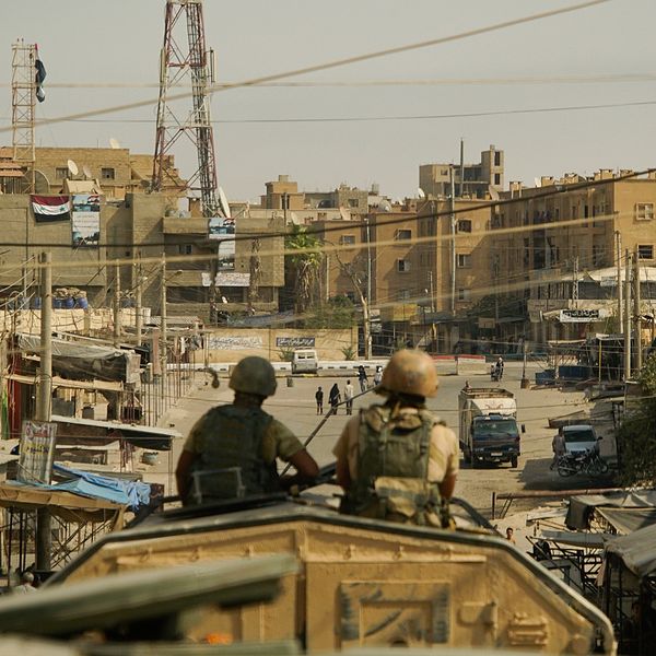 Två män i en stridsvagn blickar ned längs en gata med sandfärgade hus i syriska Deir Ezzor.