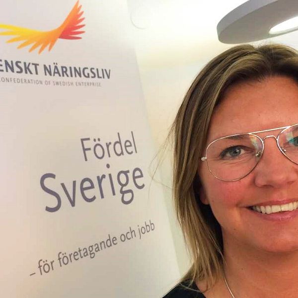 På bilden syns en kvinna med glasögon. Bakom henne finns en skärm som det står Svenskt Näringsliv på.