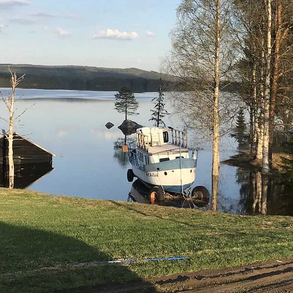 vy över grässlänt ner mot översvämmad sjö, lada i vatten, båt på vagn