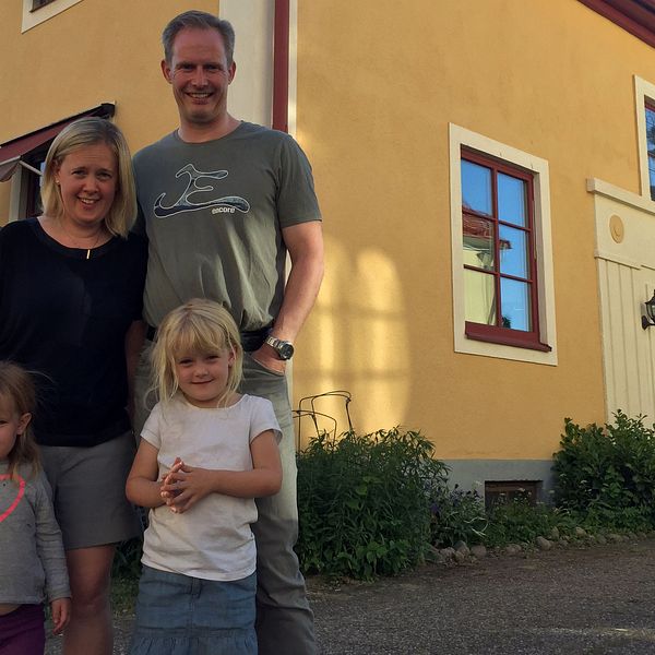 Tvåbarnsfamilj står framför gult hus.