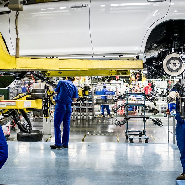 Fabriksarbetare i blå kläder monterar bilar i en fabrik.