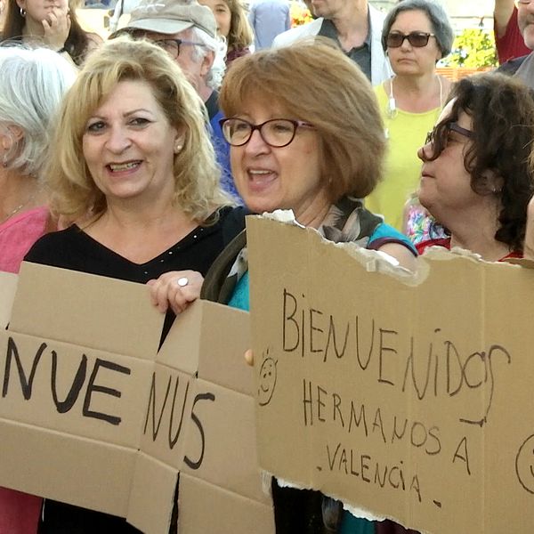 I Valencias hamn har folk samlats för att ta emot fartyget Aquarius. En grupp kvinnor tillverkar skyltar där det står ”Välkomna!”.