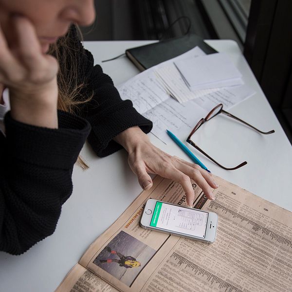 Kvinna som sitter med en tidning och en app.