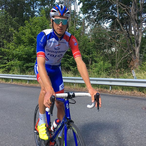 Tävlingsklädd cyklist i blått, vitt och rött på blå racercykel