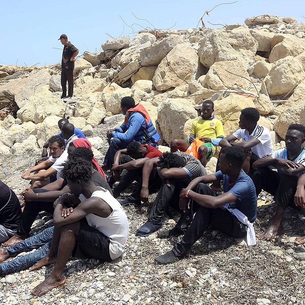 Migranter som räddades av den libyska kustbevakningen sitter på land öster om Tripoli.