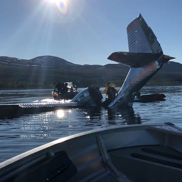 delar flygplan sticker upp ur sjö, båt med folk på intill