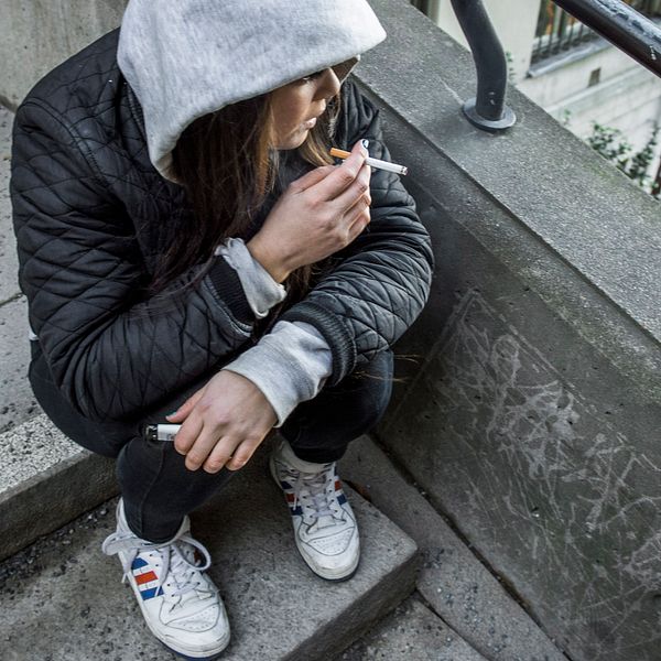 tonårstjej sitter på en trappa och röker en cigarett.