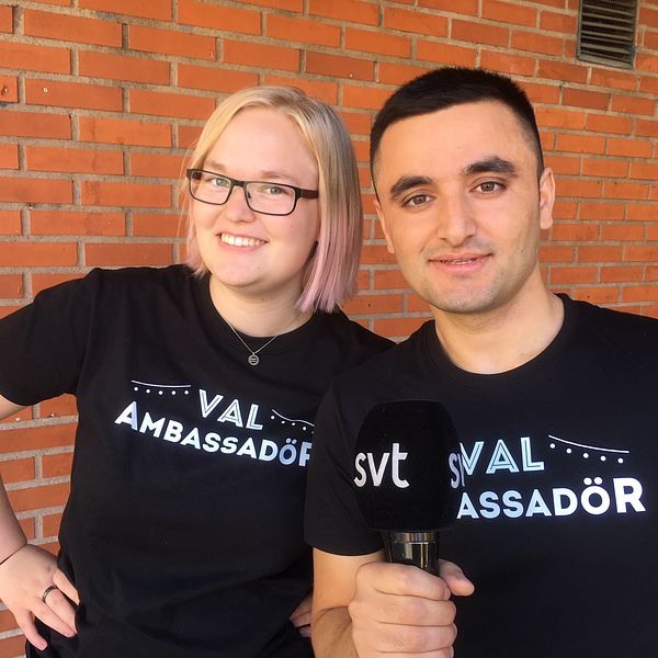 en tjej och en kille framför en tegelvägg, i t-shirtar med texten ”val-ambassadör”