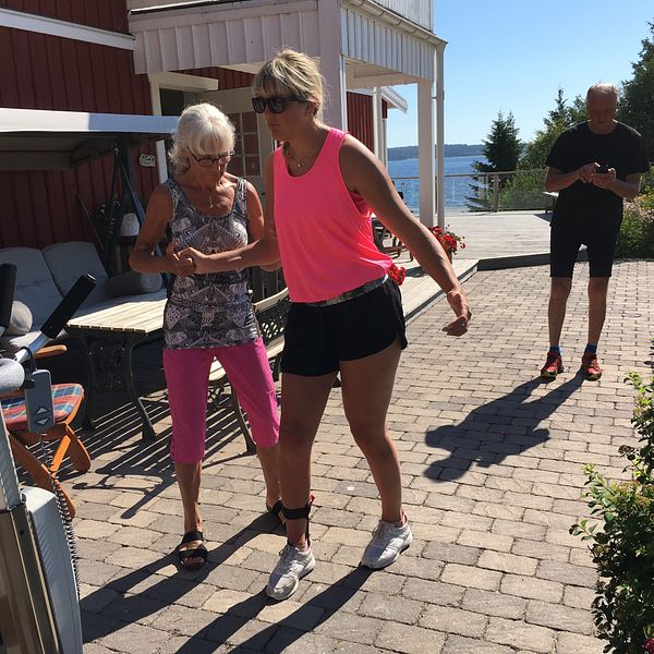 Anna får hjälp av sin mor att gå vid hus vid havet, sommar och sol