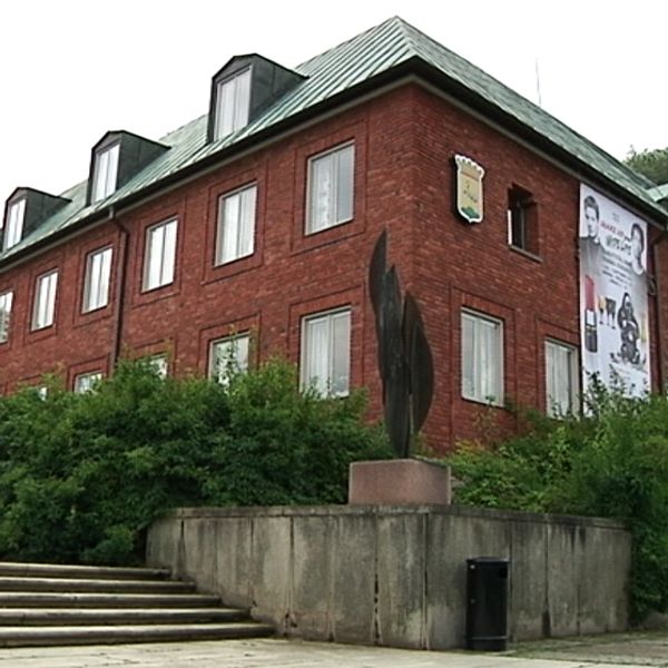Röd tegelbyggnad med flera våningar och en modern skulptur i förgrunden.