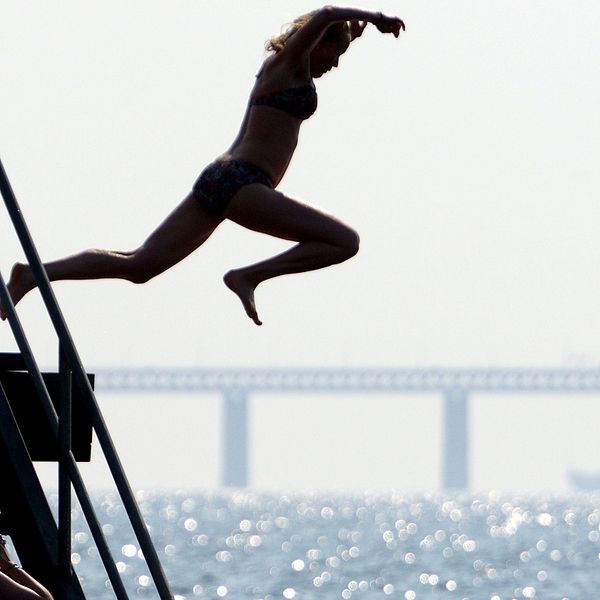 En kvinna hoppar i vattnet vid Västra Hamnen i Malmö med Öresundsbron som bakgrund