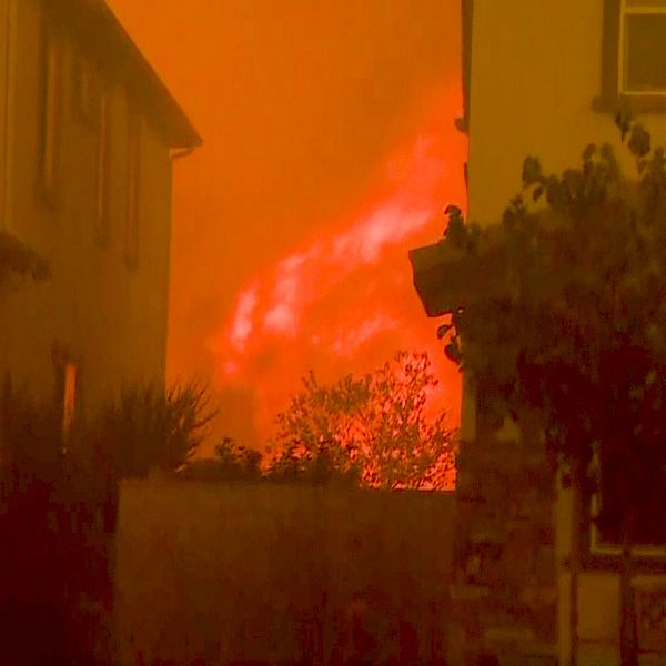 Två bostadshus med stora eldsflammor mellan och bakom husen.