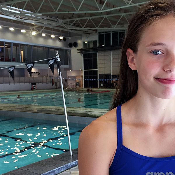 15-årig tjej i baddräkt står vid en simbassäng.