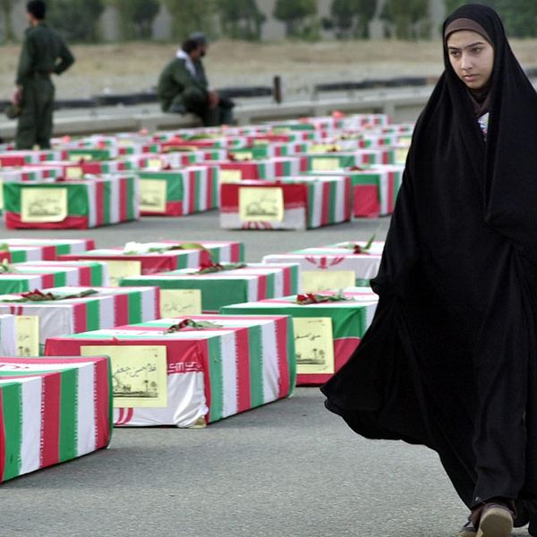 En kvinna i chador passerar kistor svepta i iranska flaggor.