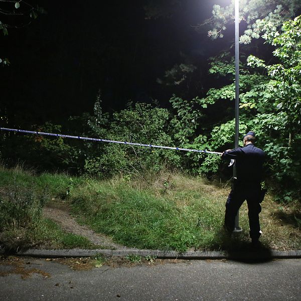En polis sätter upp avspärrningsband vid ett mörkt skogsparti.