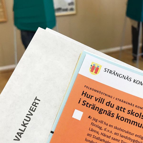 Valsedel och  valkuvert, i bakgrunden syns två röstskynken i vallokalen i Härad i Strängnäs