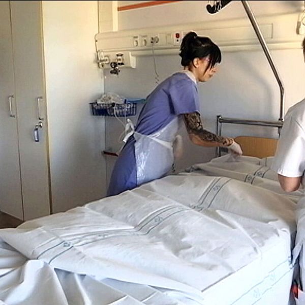 Två kvinnliga undersköterskor hjälps åt att bädda en sjukhus säng