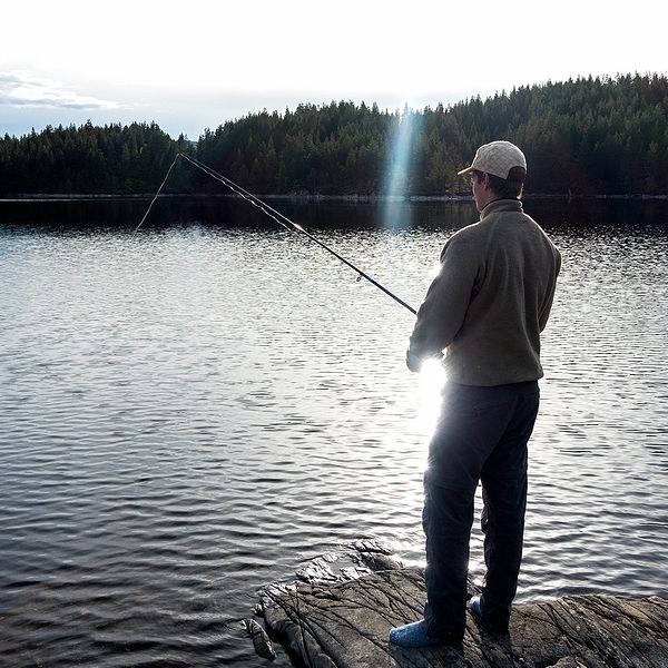 En man står vid ett vattendrag och fiskar.