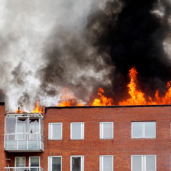 Ett rött tegelhus där stora eldslågor slår ut från taket.
