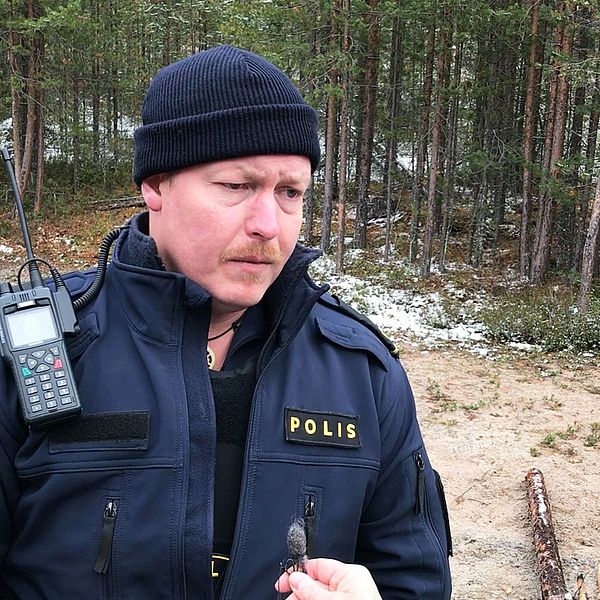 en man i polisuniform fotad på en öppen plats med skog bakom