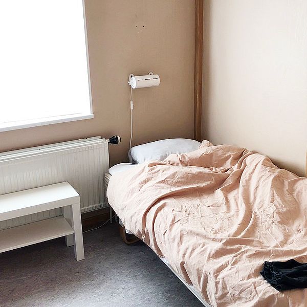 En enkel säng i ett spartanskt inrett rum med ett stort ljust fönster med motljus. Bilden är tagen i Stadsmissionens härbärge i Eskilstuna.