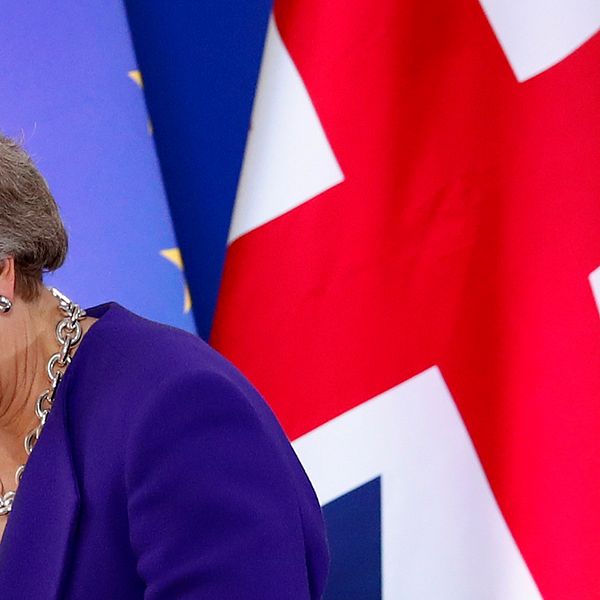 Theresa May tittar ner. I bakgrunden syns Storbritanniens och EU:s flaggor.