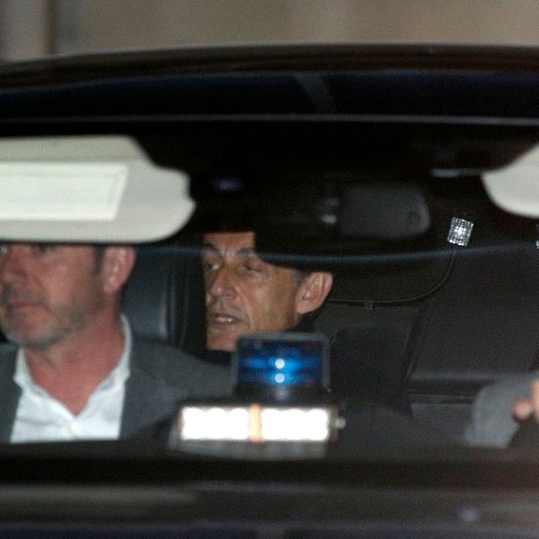 Frankrikes tidigare president Nicolas Sarkozy skymtar i baksätet i en polisbil. Bilden är från i mars i år när han förhördes på en polisstation i Nanterre utanför Paris.