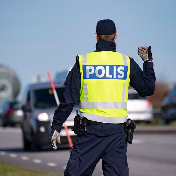 En polis vinkar åt bilar vid en väg.