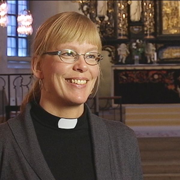 en leende kvinna i prästkläder, i en kyrka