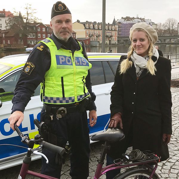 Polisen Tomas Bonn håller i en cykel bredvid reportern Otilia Bogen framför en polisbil vid Eskilstunaån.