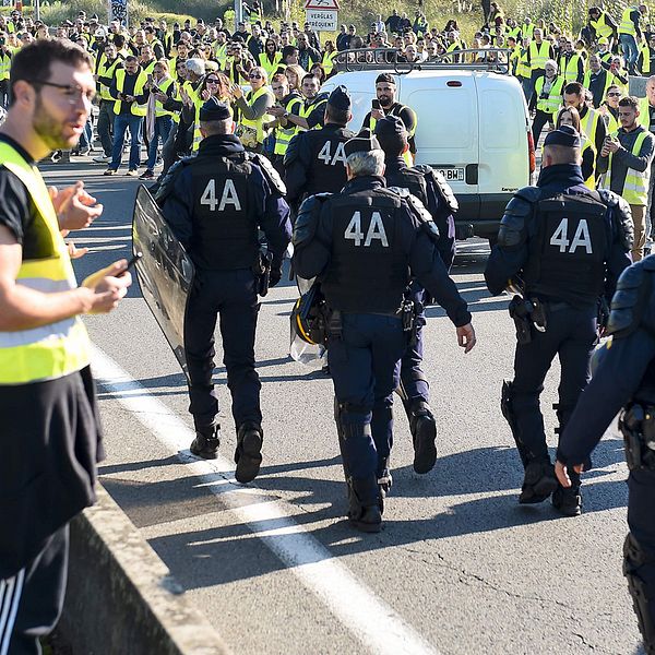 Polis marscherar genom en korsning som blockeras av ”gula västarna”.