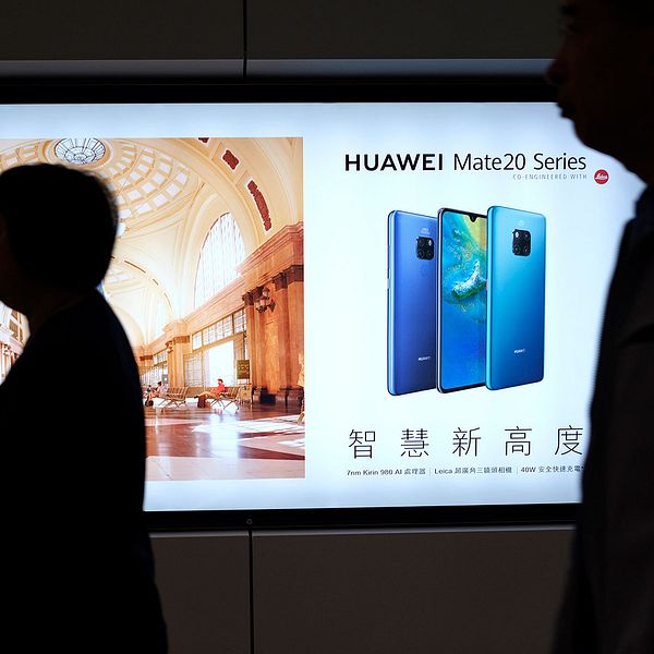 Människor framför reklam för Huawei i Hongkongs tunnelbana