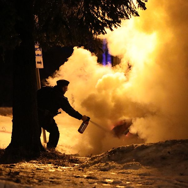 kvällstid vinter, polisman som sprutar med brandsläckare på kraftigt rykande bil