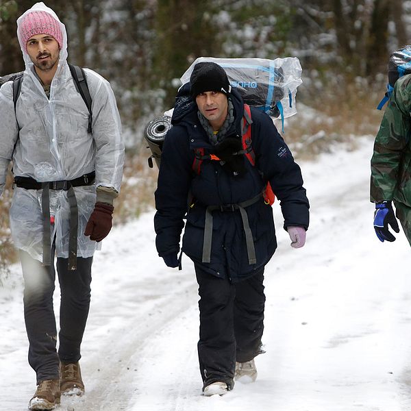 Tre män bär på sin packning i snön på väg mot gränsen till Kroatien.