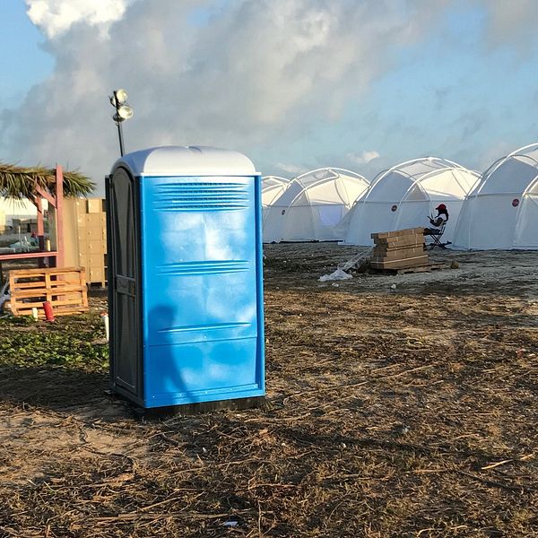 Blå bajamaja framför vita tält på en öppen gräsyta under molnig himmel.